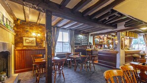 A traditional pub interior with exposed wooden beams, brick walls, and a bar area with a variety of bottles. - The Forest Lodge (Mansfield)