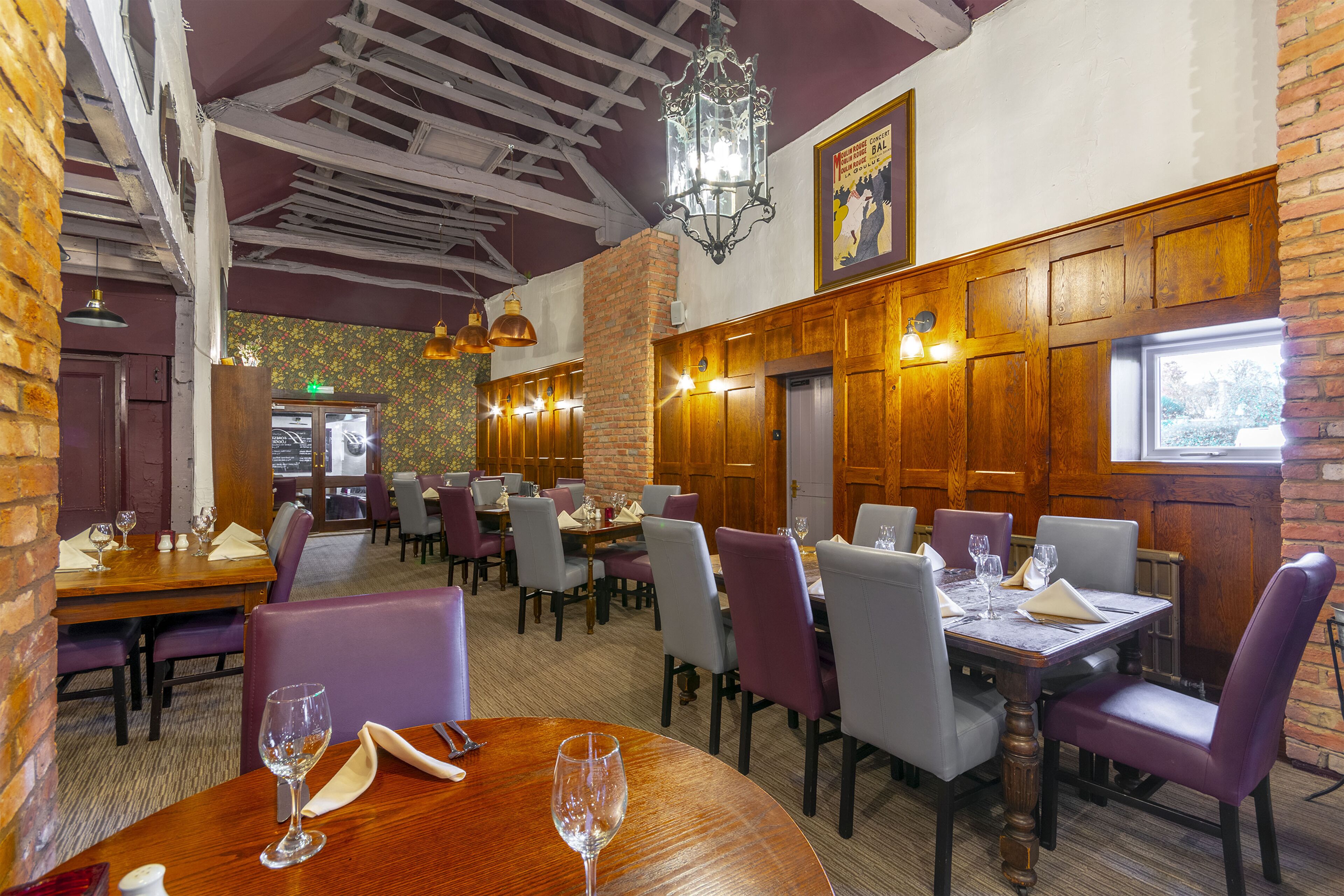 A restaurant interior with wooden tables and chairs, a brick wall, and hanging lights.