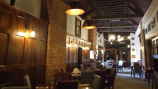 A restaurant interior with brick walls, wooden paneling, and hanging pendant lights. Tables are set with chairs, and there are multiple dining areas visible. - The Forest Lodge (Mansfield)