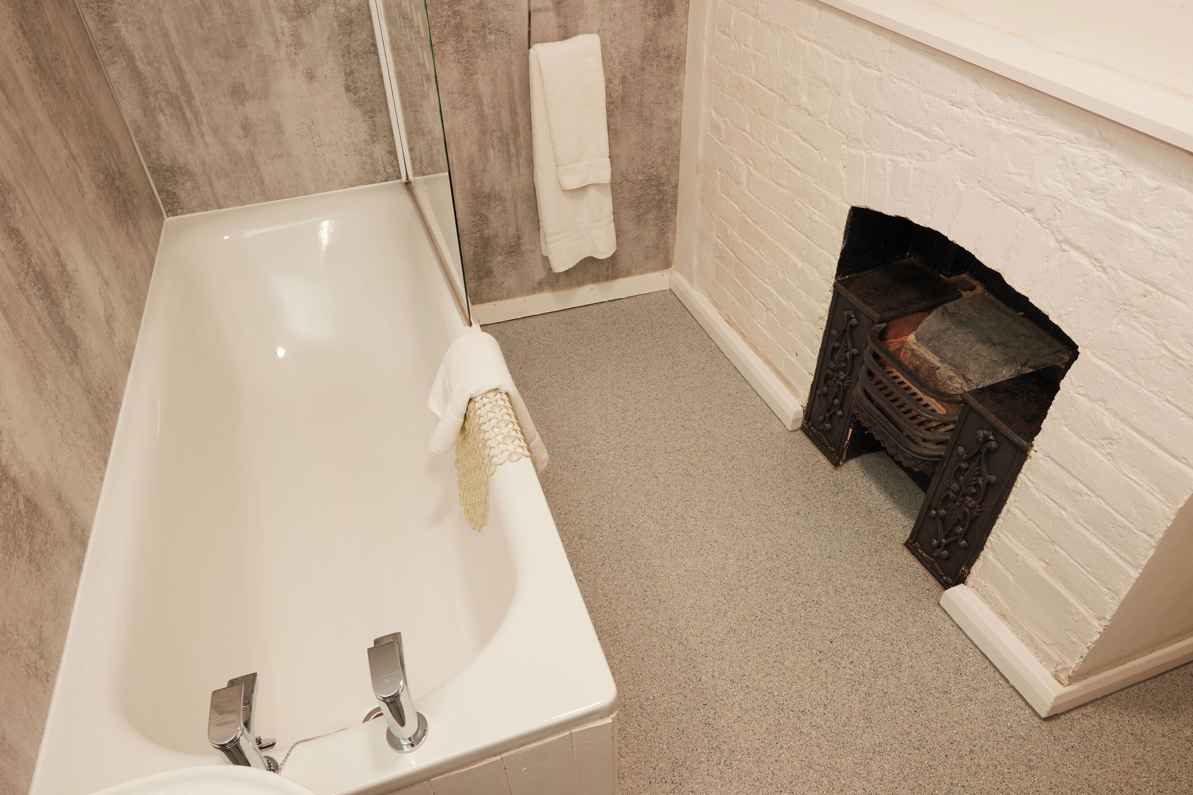 A bathroom with a bathtub, a white towel, a glass shower enclosure, and a fireplace.