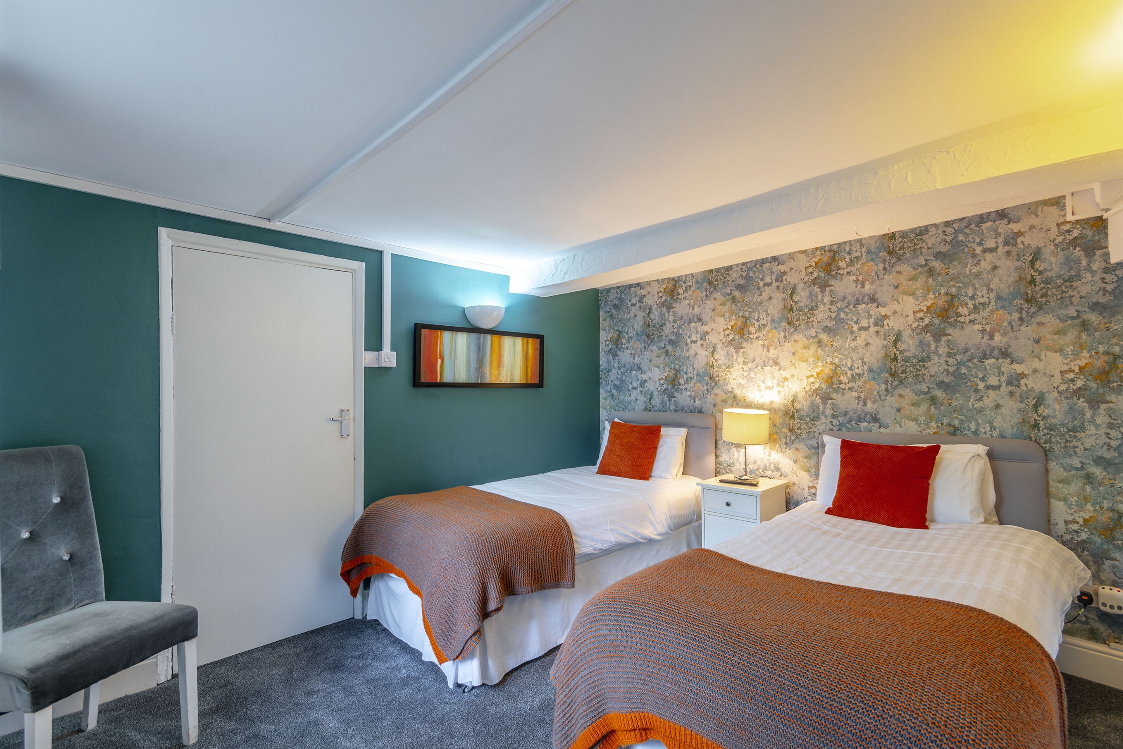Ein Zimmer mit zwei Betten, einem Stuhl, einer Tür und einer blumengemusterten Wand.