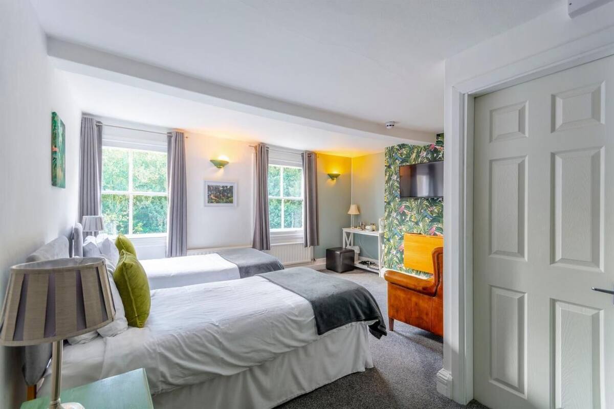 A hotel room with two beds, a desk, a chair, a TV, and a window with curtains.
