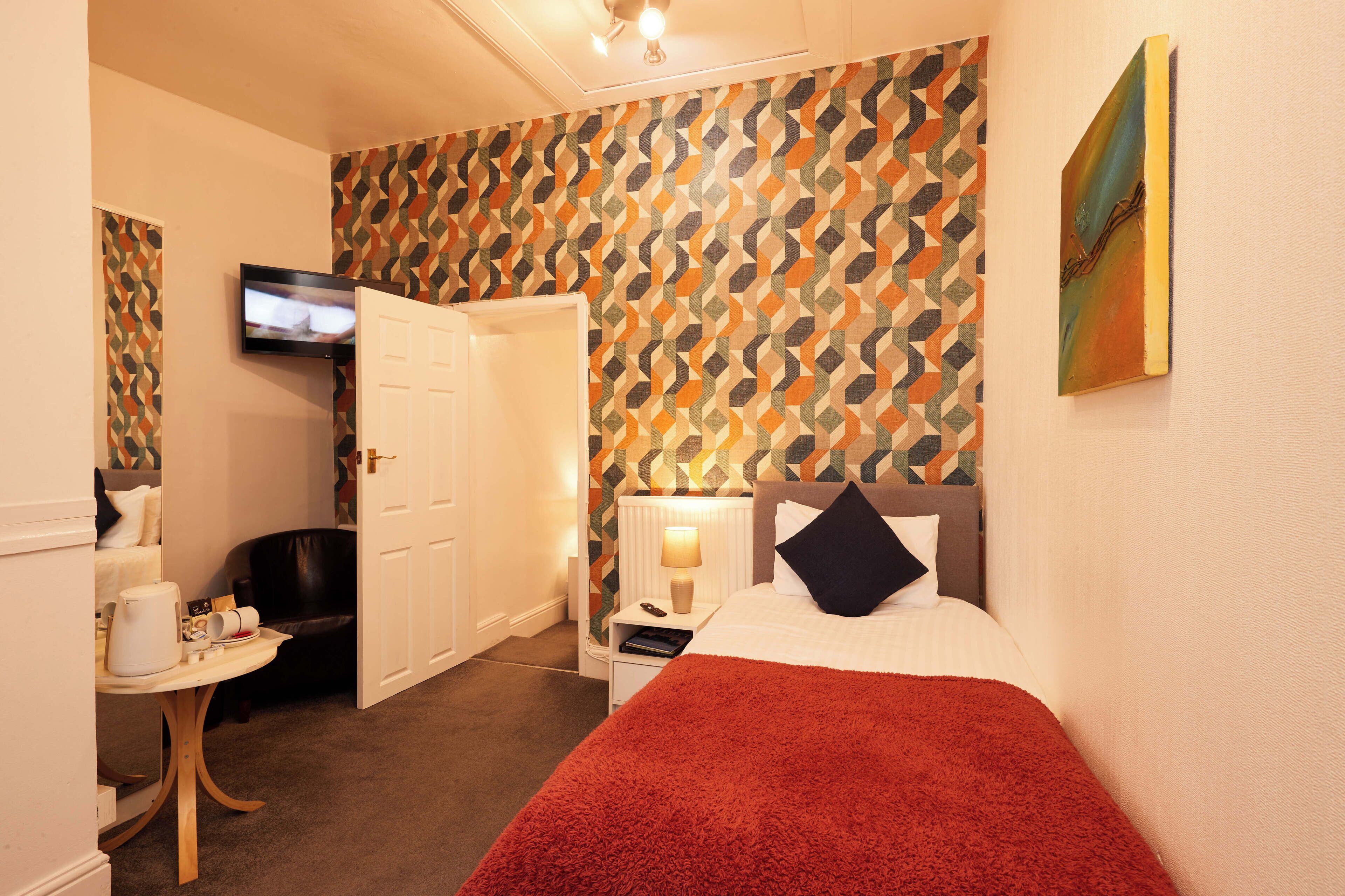 A hotel room with a bed, a desk, a chair, a television, and a patterned wall.