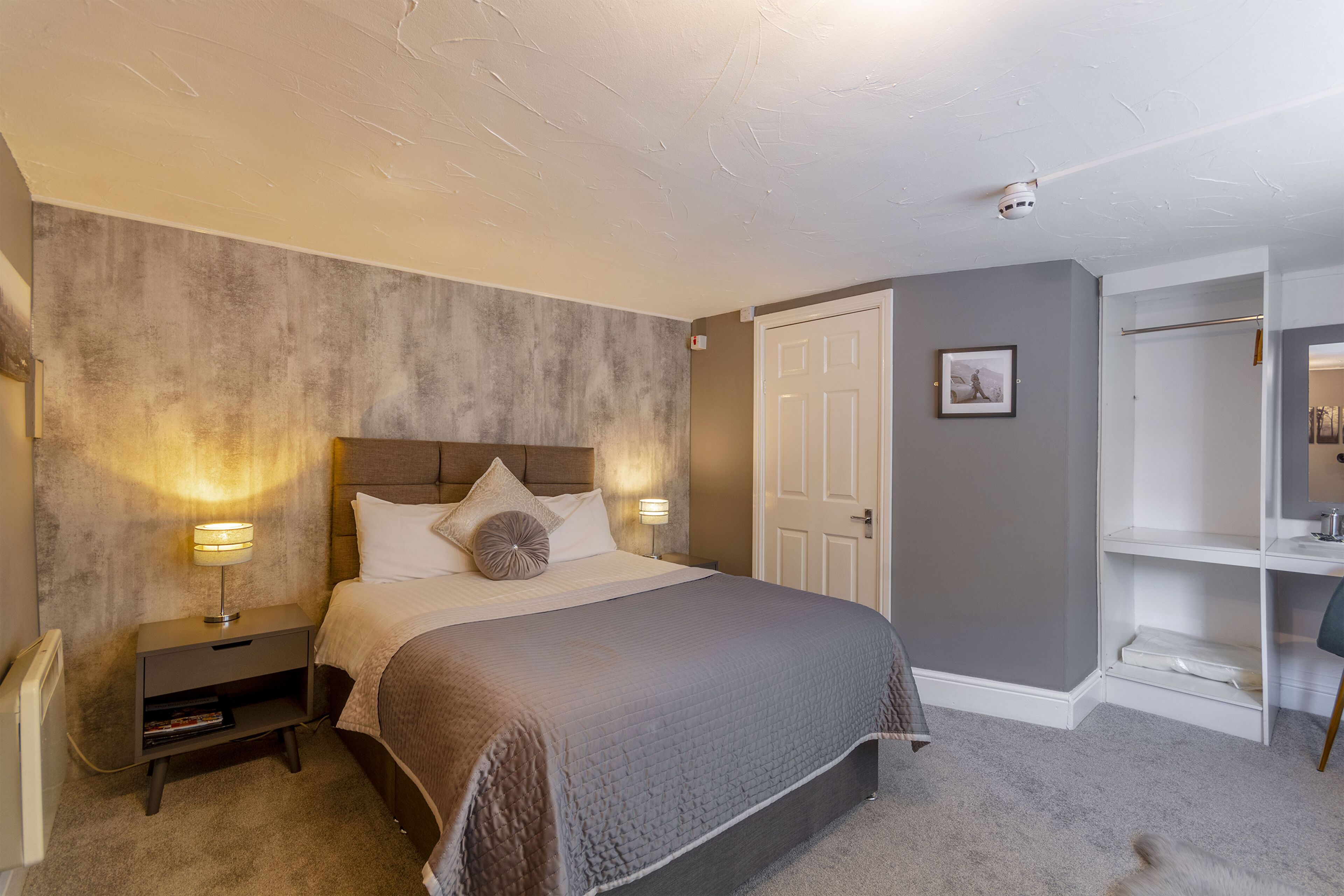A bedroom with a bed, bedside lamps, a nightstand, a wardrobe, and a small desk with a chair.