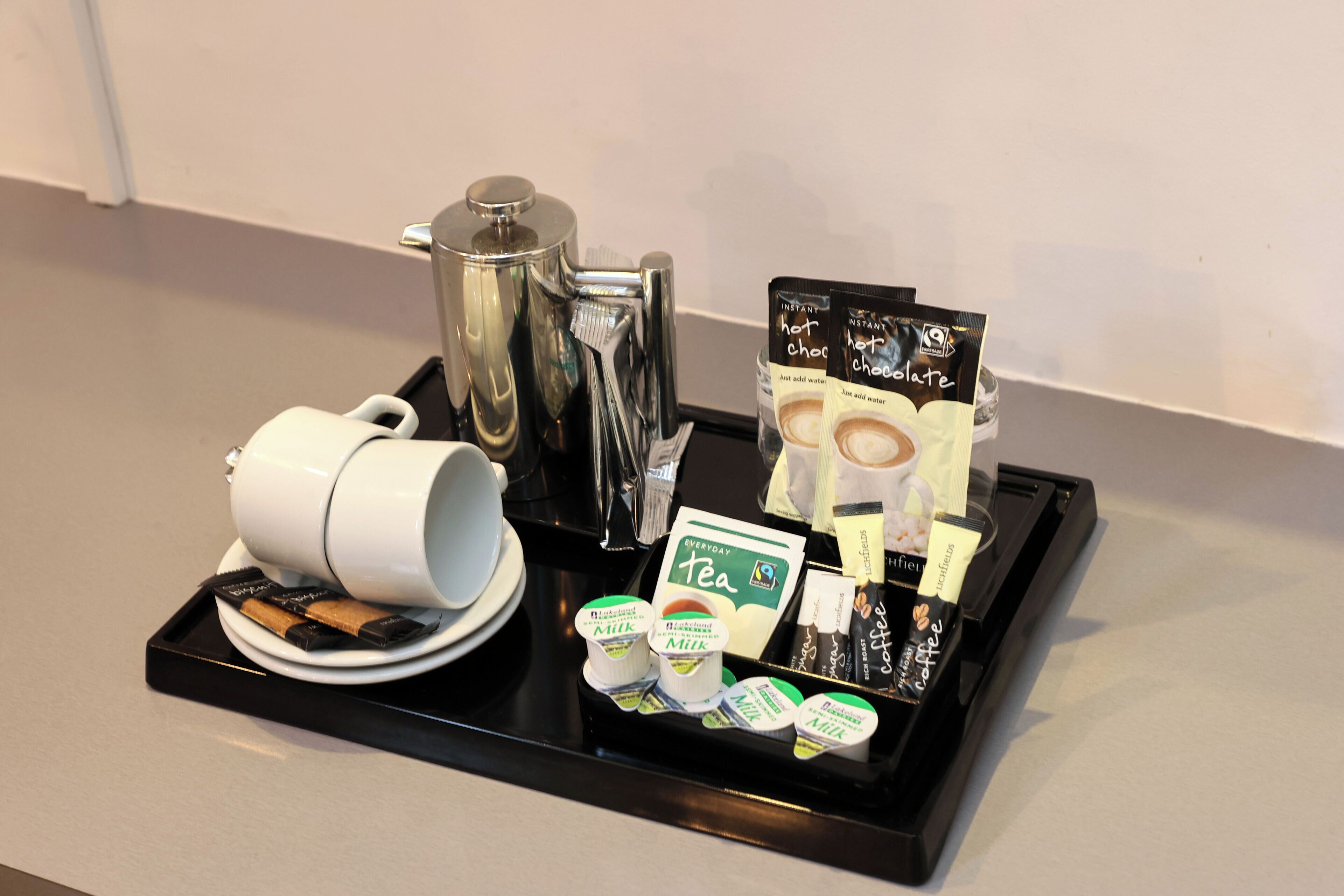 Un vassoio con una macchina da caffè, una tazza bianca, bustine di tè e confezioni di latte.