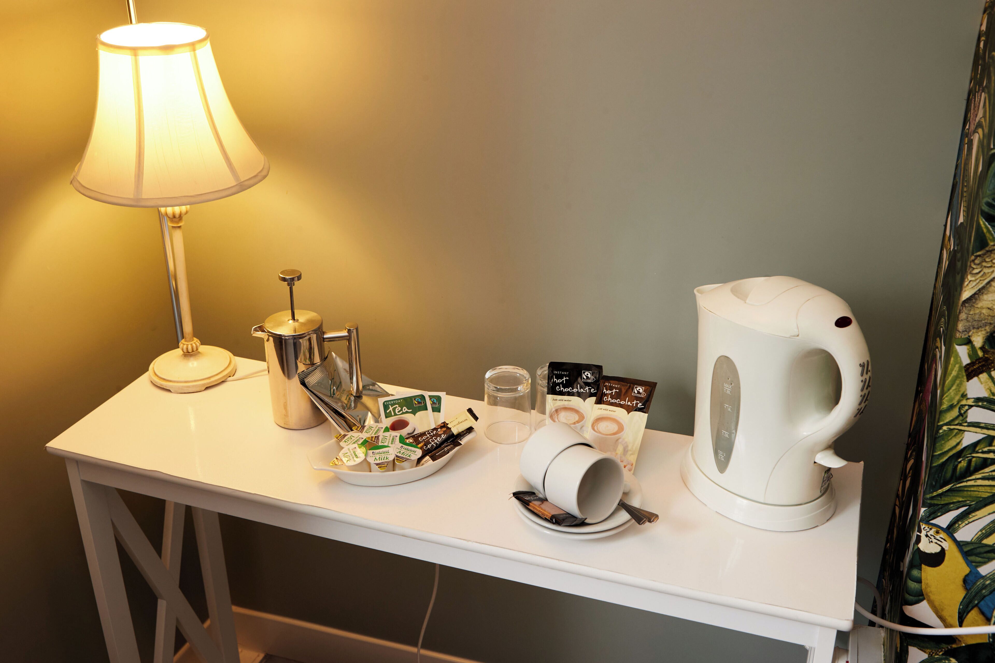 A white table with a lamp, a kettle, a tea set, and some packaged snacks.