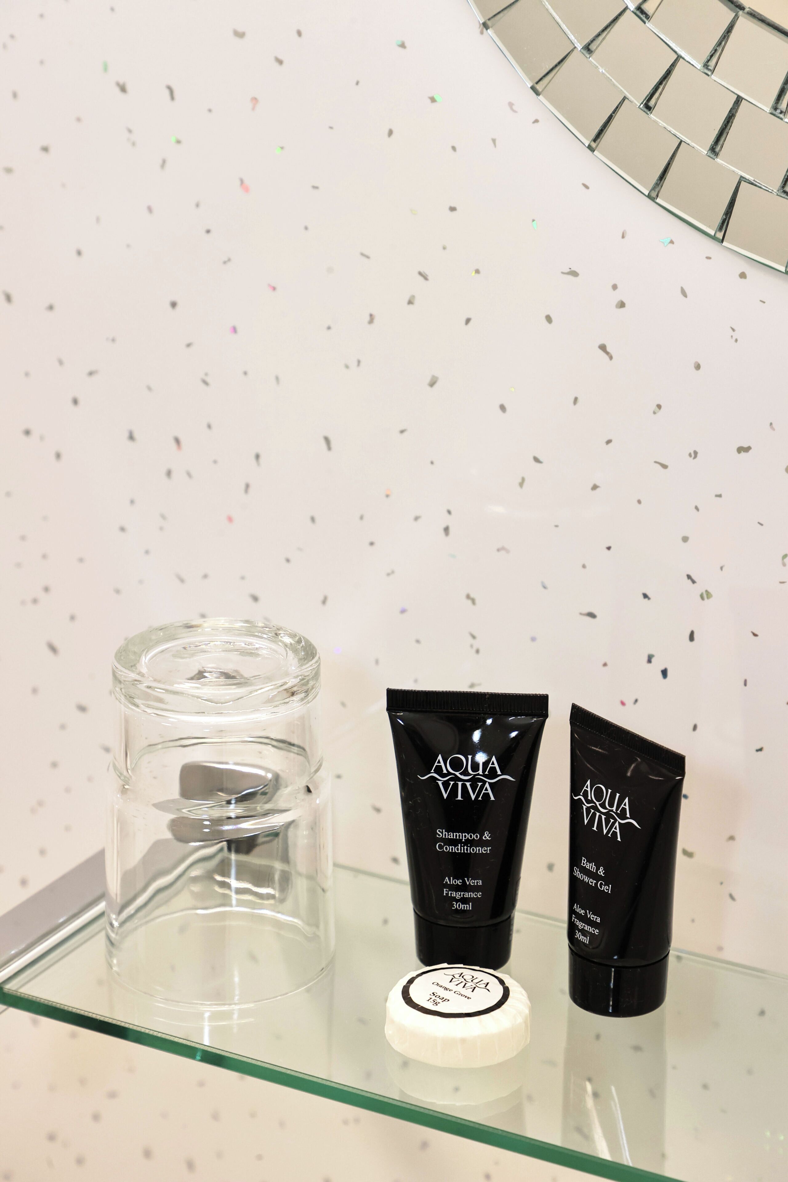 A bathroom shelf with a clear glass container, two black bottles labeled 'AQUA VIVA', and a white lid.
