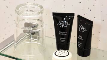 A bathroom shelf with a clear glass container, two black bottles labeled 'AQUA VIVA', and a white lid.