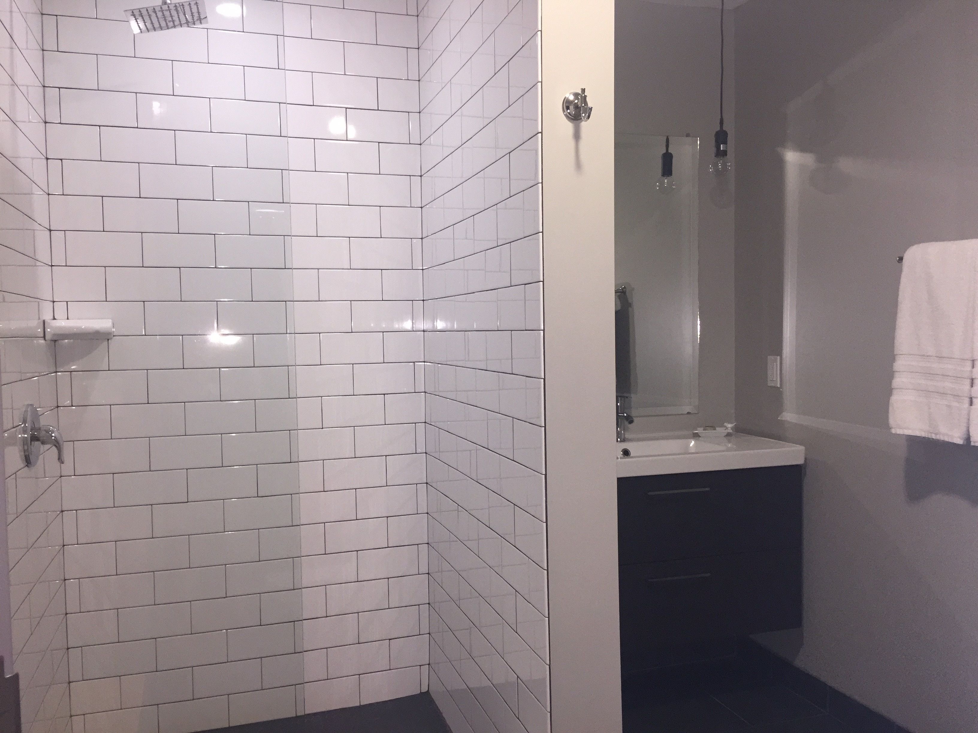Un baño con paredes de azulejos blancos, cabina de ducha de vidrio, lavamanos y una toalla colgada en la pared.