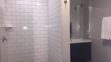 A bathroom with white tiled walls, a glass shower enclosure, a sink, and a towel hanging on the wall.