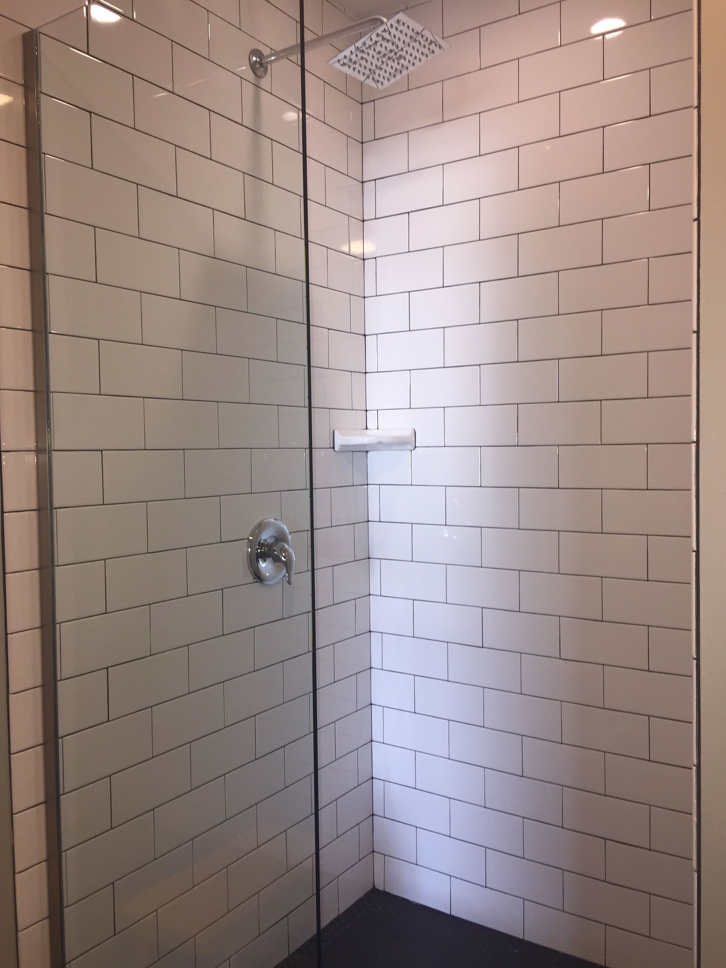 A shower area with white tiled walls and a glass door.