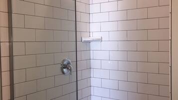 A shower area with white tiled walls and a glass door.