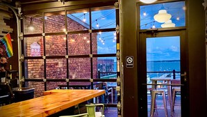 A restaurant with a brick wall, large windows, and a wooden table. - Hotel Kilbourne Downtown Sandusky (Sandusky)
