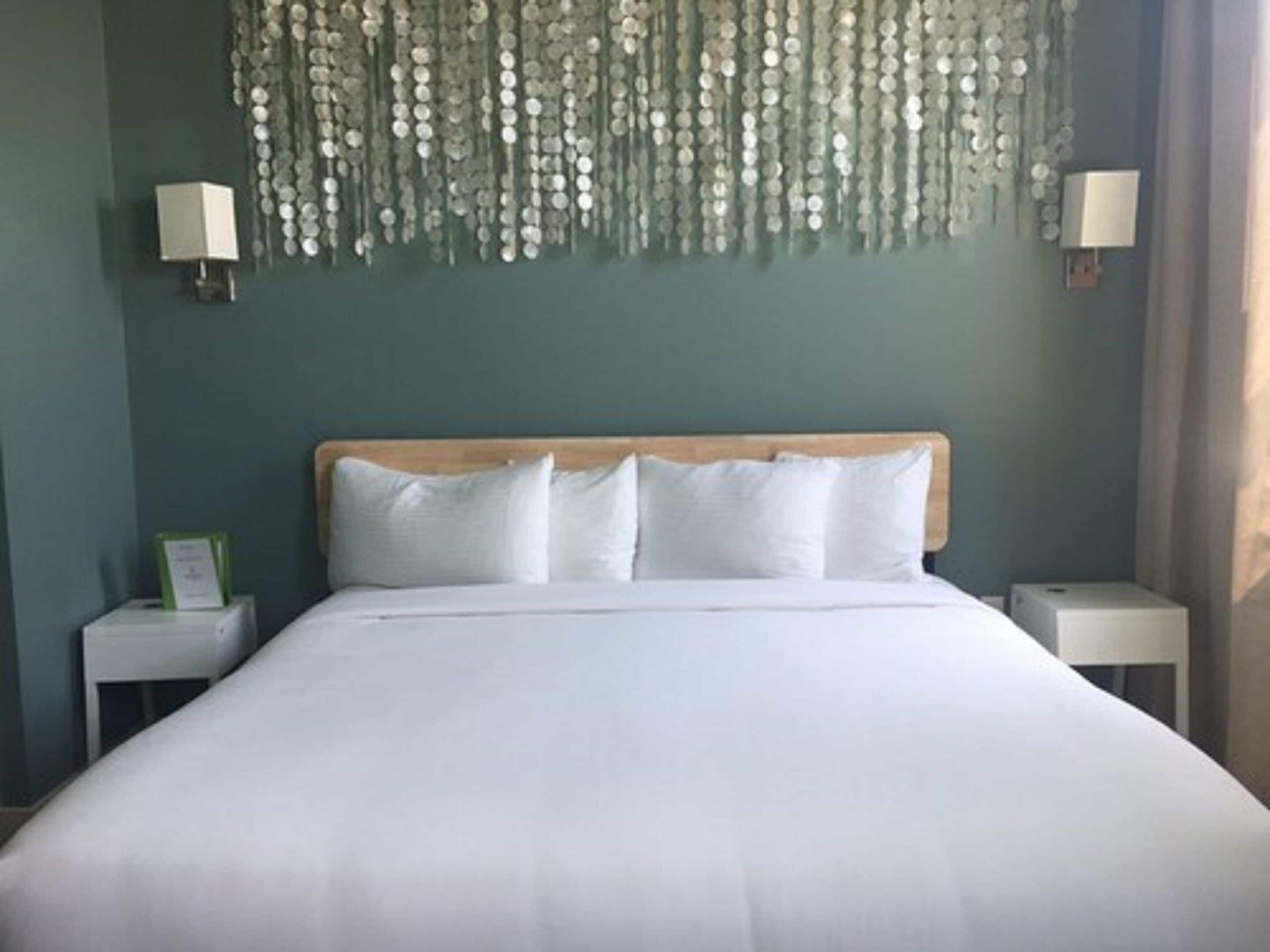 Una habitación de hotel con una cama grande, dos mesitas de noche y una lámpara decorativa colgante.