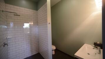 A bathroom with white tiled walls, a shower area, a toilet, and a sink with a mirror.