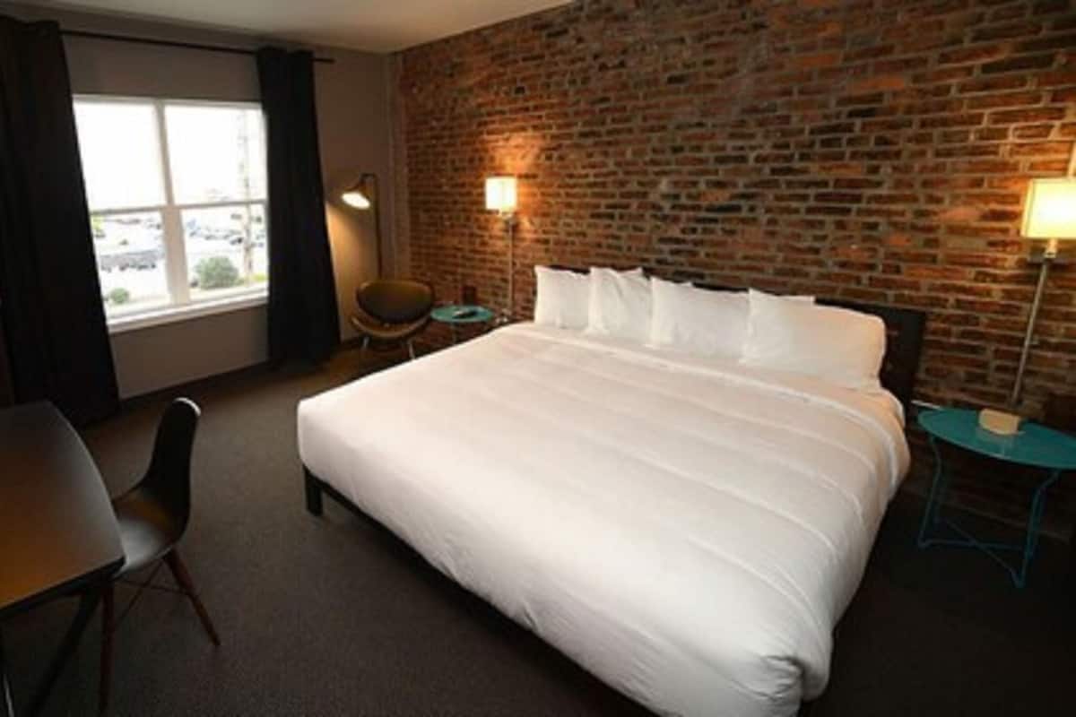 Une chambre d’hôtel avec un grand lit, un bureau, une chaise et un mur en briques.