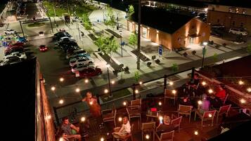 Un bar en la azotea con mesas al aire libre, con vistas a un estacionamiento y un edificio de columnas.