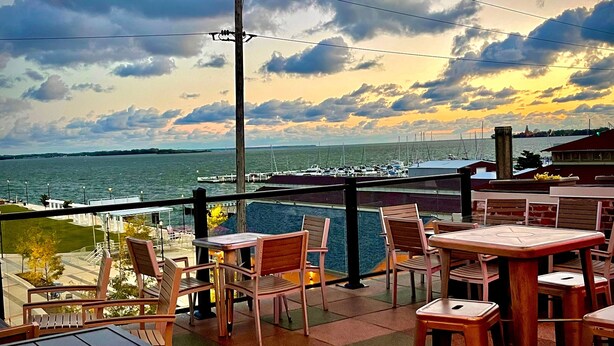 An outdoor seating area with tables and chairs, overlooking a marina with boats and a view of the water. - Hotel Kilbourne Downtown Sandusky (Sandusky)