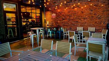 An outdoor seating area with tables and chairs, a brick wall, and string lights.