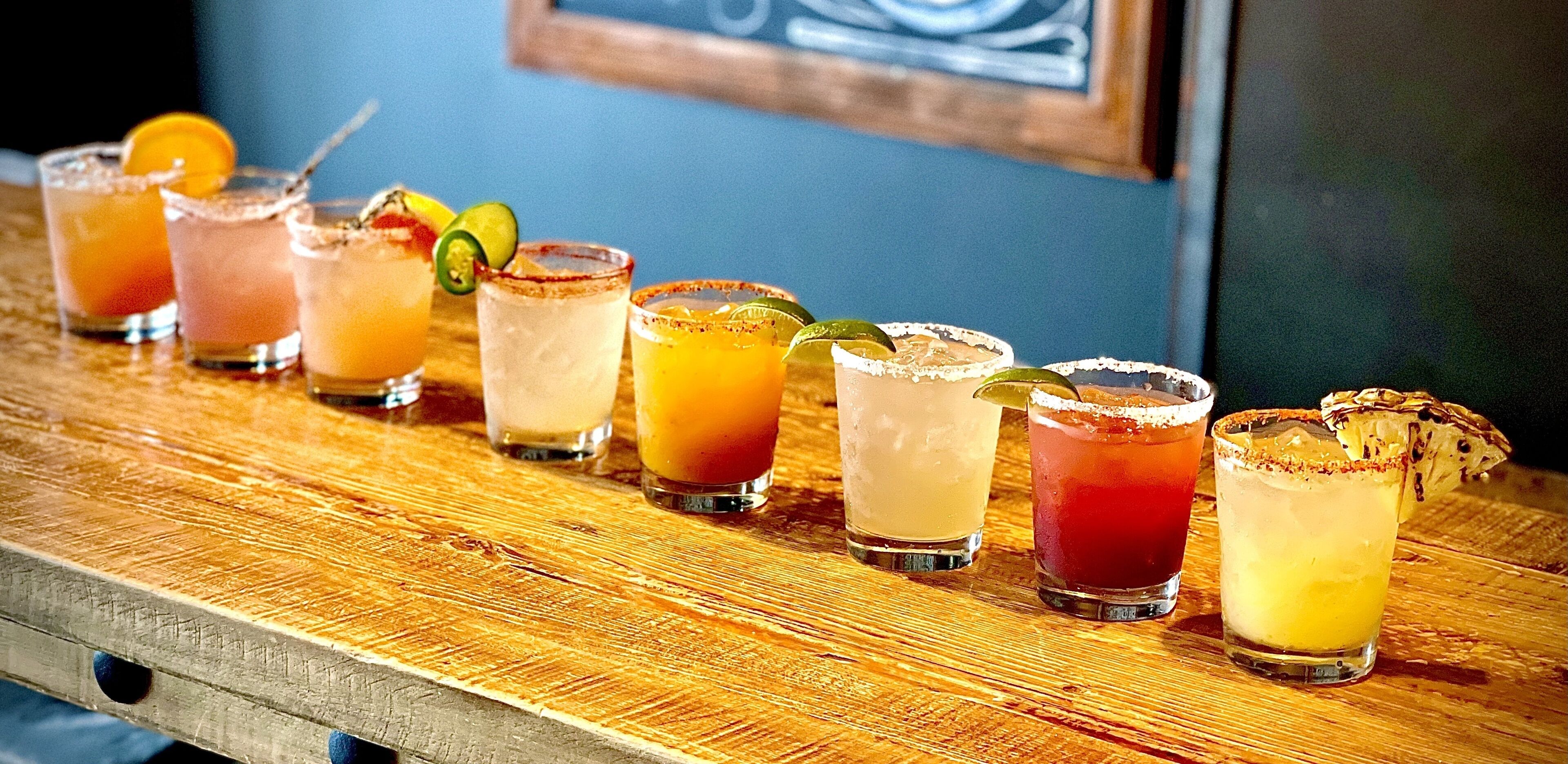 A bar with various cocktails, some garnished with lime and others with a salted rim.
