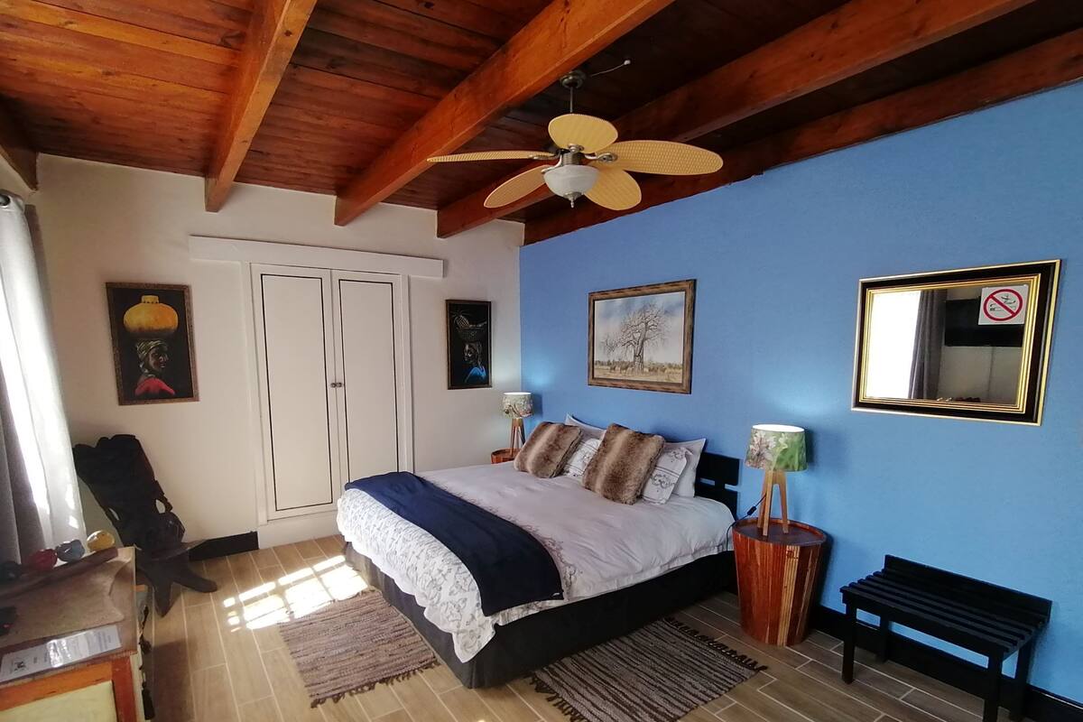 Un dormitorio con cama, ventilador de techo, banca, espejo y obras de arte en las paredes.