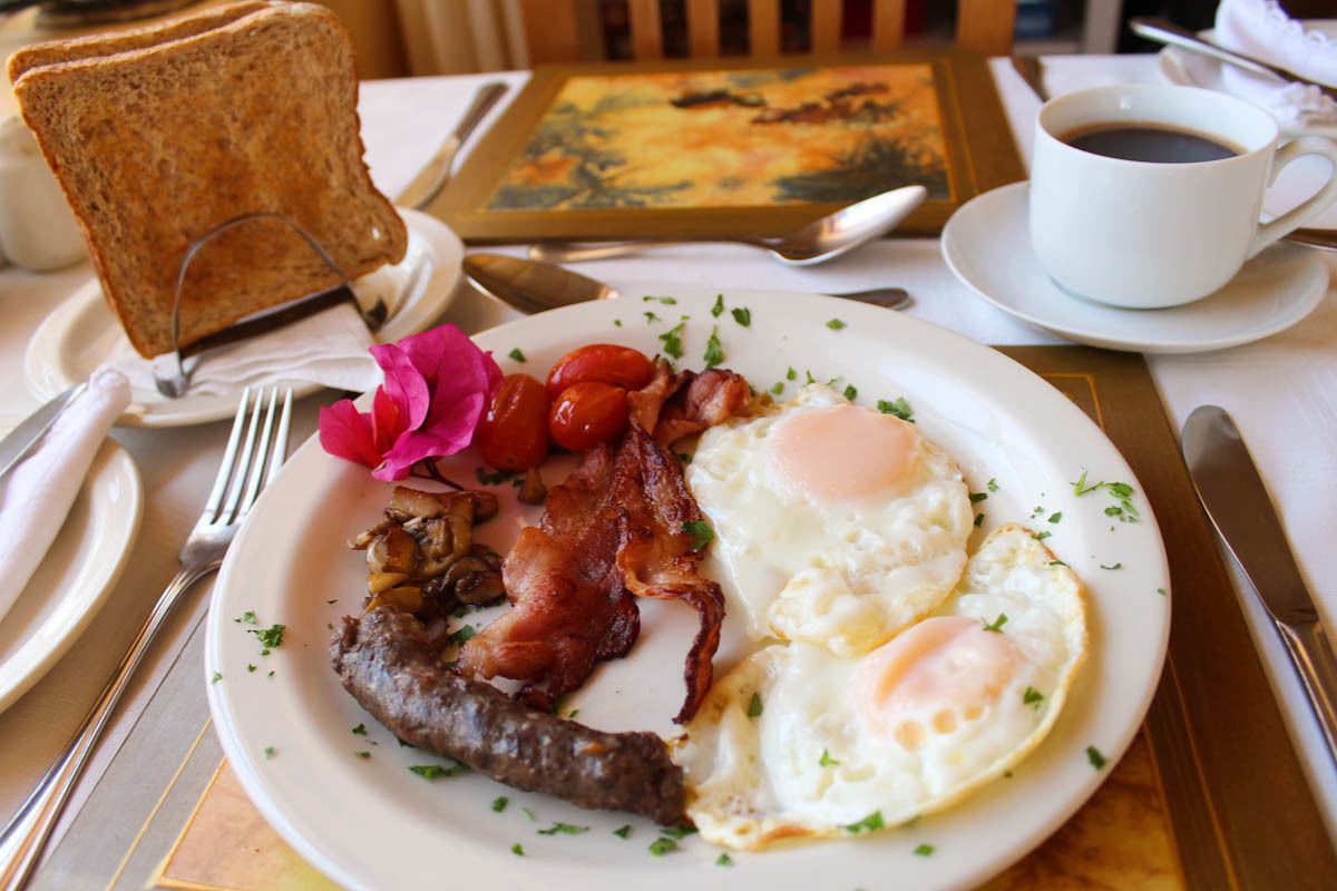 A breakfast plate with eggs, bacon, tomatoes, and toast, accompanied by a cup of coffee and a painting.