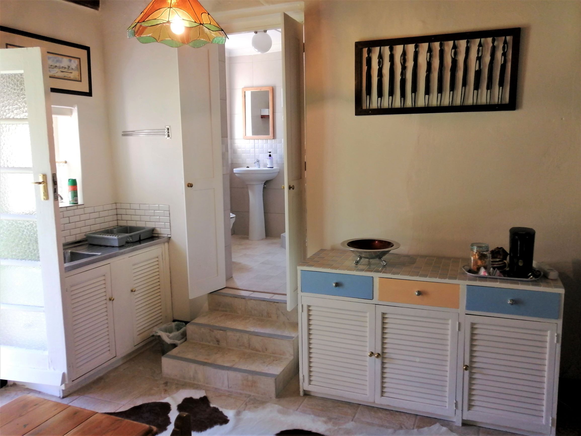 Cocina con gabinetes blancos, un lavamanos y una encimera. Una escalera conduce a un baño.