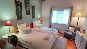 A bedroom with two beds, a wooden ceiling, a window with curtains, and a nightstand with a lamp.