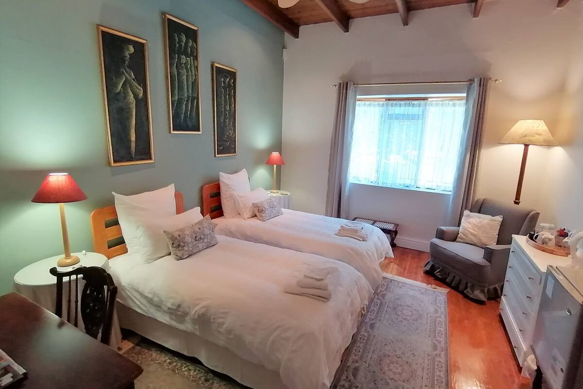 Un dormitorio con dos camas, techo de madera, ventana con cortinas y una mesita de noche con lámpara.