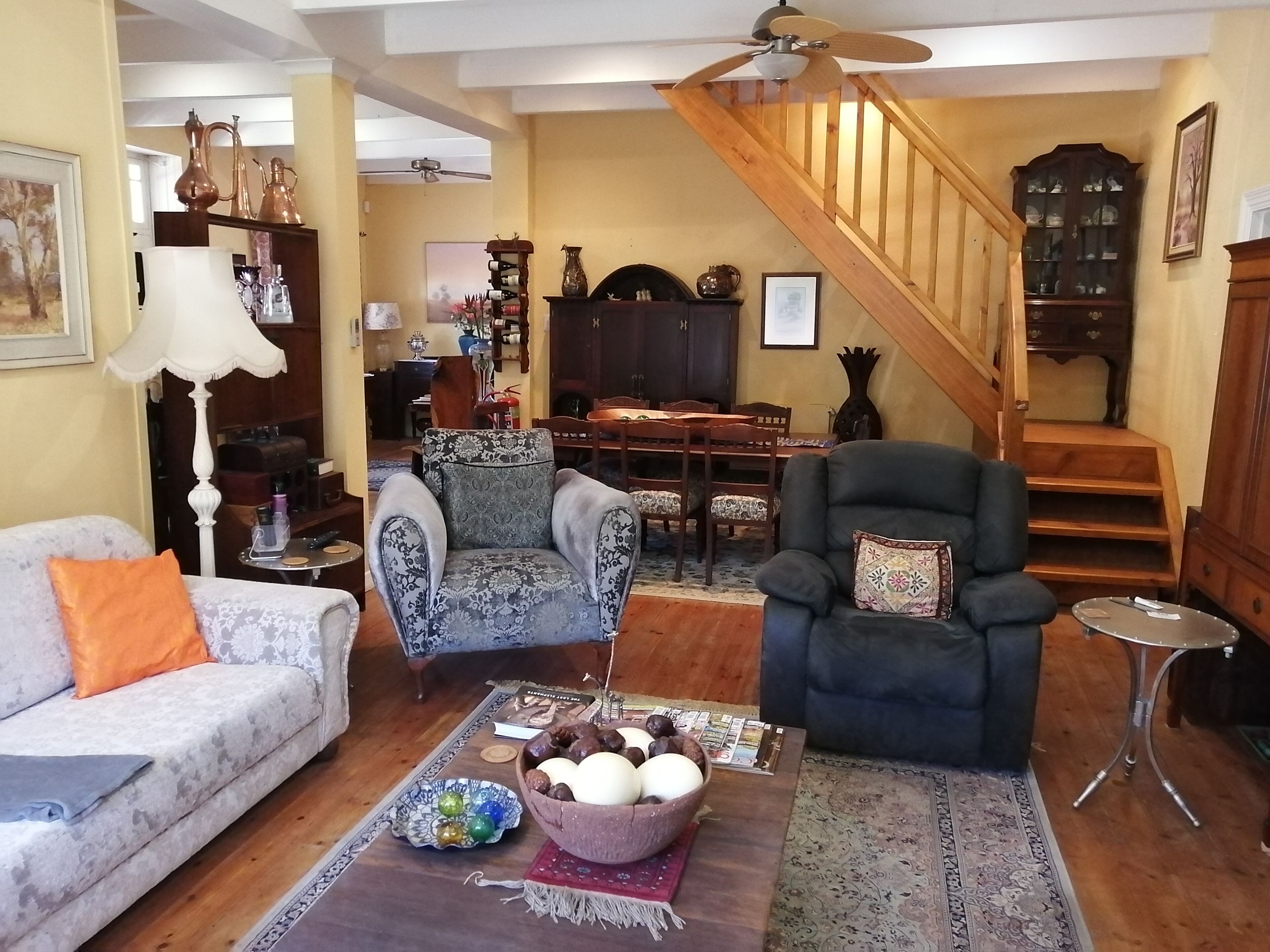 A living room with a sofa, armchairs, a dining table, and a staircase.