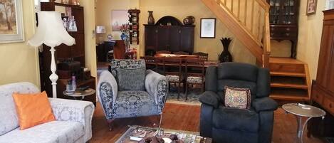 A living room with a sofa, armchairs, a dining table, and a staircase.