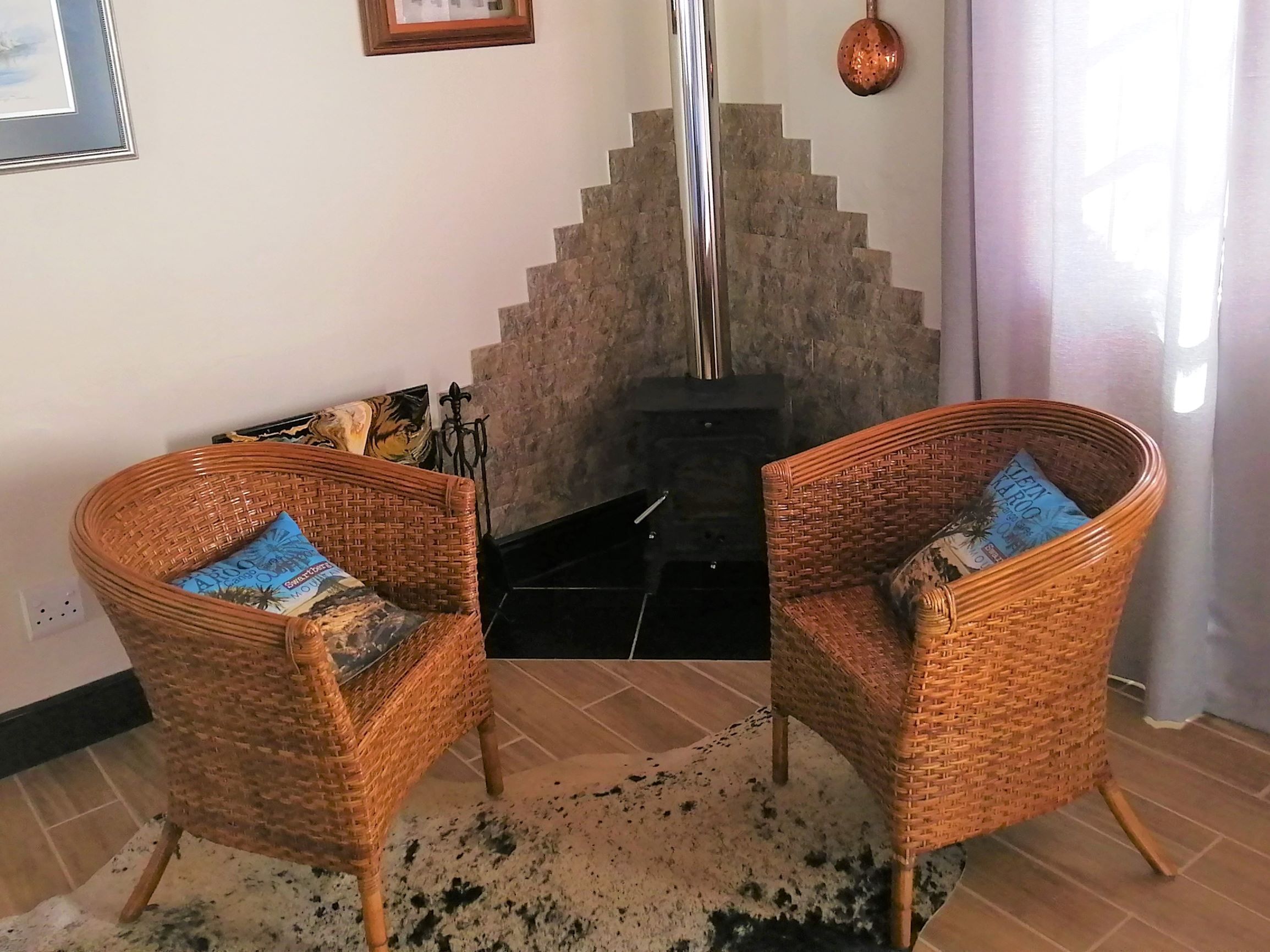 Dos sillas de mimbre con cojines azules, una chimenea y una pared de piedra.