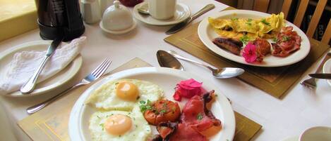A breakfast setting with plates of eggs, bacon, and sausages, a coffee maker, and condiments on a table.