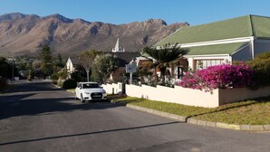 A street with a white car parked on the side, a building with a green roof, and mountains in the background.