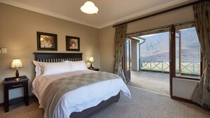 A bedroom with a large bed, two bedside tables with lamps, a view of the outdoors through a sliding door, and two framed pictures on the wall. - Dynasty Red Mountain Ranch (Clarens)