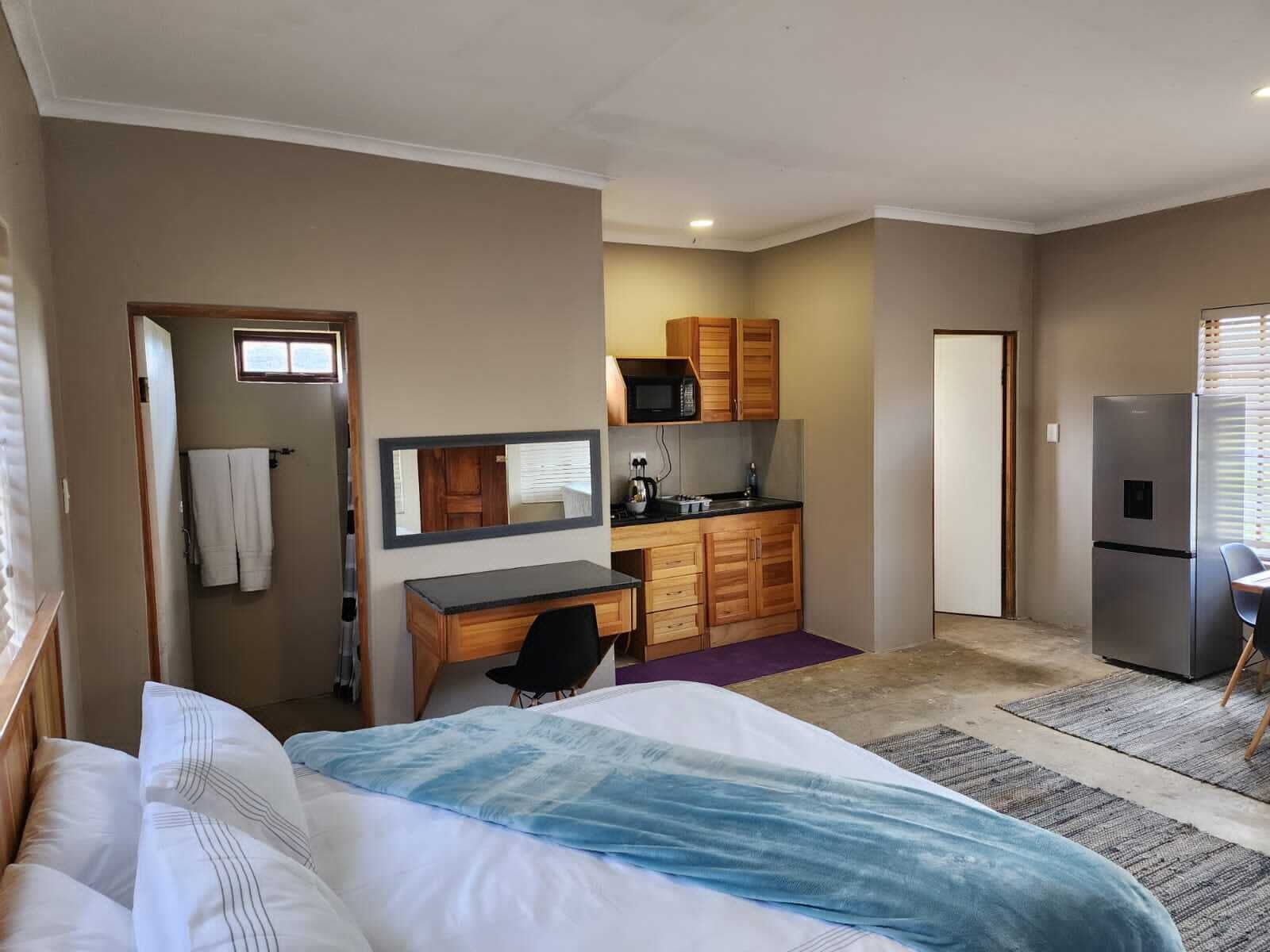 A compact hotel room with a bed, a desk, a kitchenette, and a refrigerator.