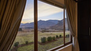 A room with a large window offering a view of a grassy field and distant mountains. - Dynasty Red Mountain Ranch (Clarens)
