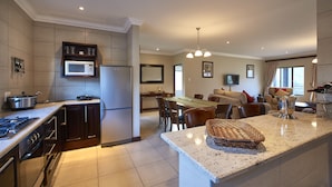 A modern kitchen with a central island, a dining area with a table and chairs, and a living room with a sofa and a TV. - Dynasty Red Mountain Ranch (Clarens)