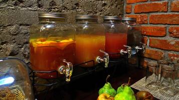 Una estación de bebidas con tres frascos de vidrio llenos de bebidas, un grifo y una mesa con frutas y vasos.