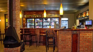 A bar area with brick walls, wooden chairs, and a large screen. - Casa Forno Country Hotel (Otjiwarongo)
