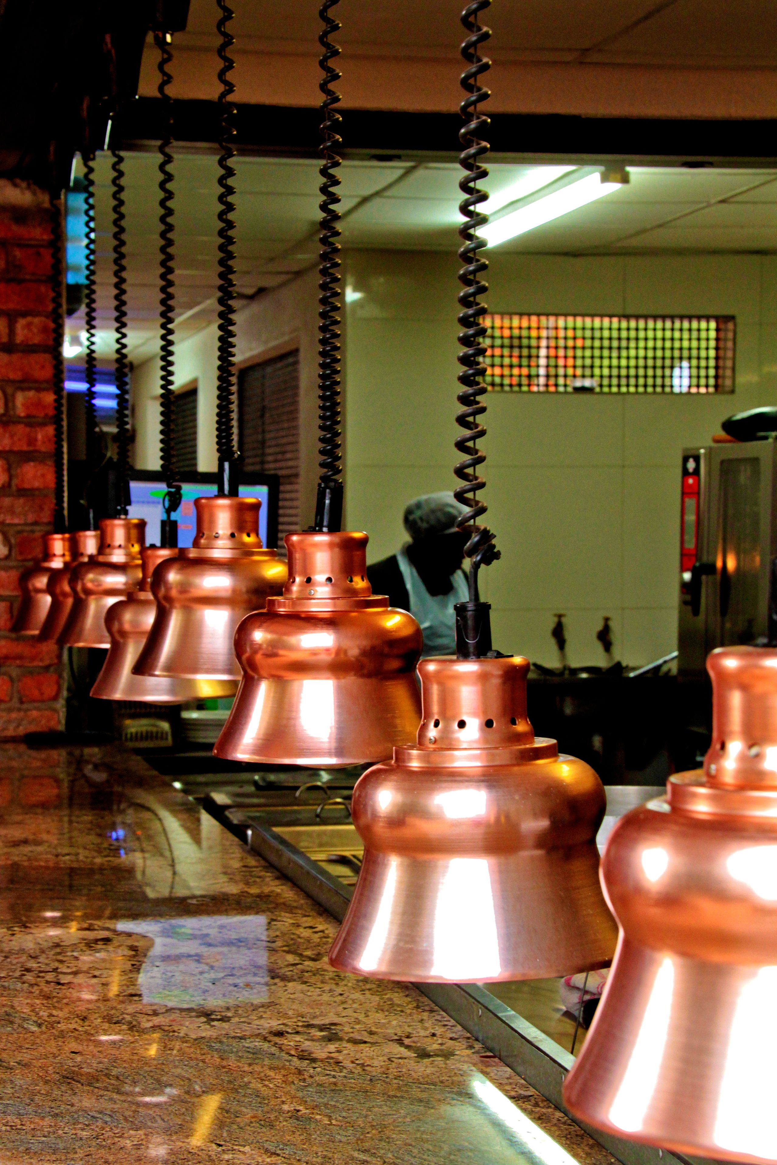 A kitchen with copper pots hanging from a ceiling, a brick wall, and a tiled backsplash.