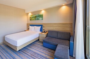 Quarto de hotel com cama, sofá, mesa de cabeceira e um quadro na parede.