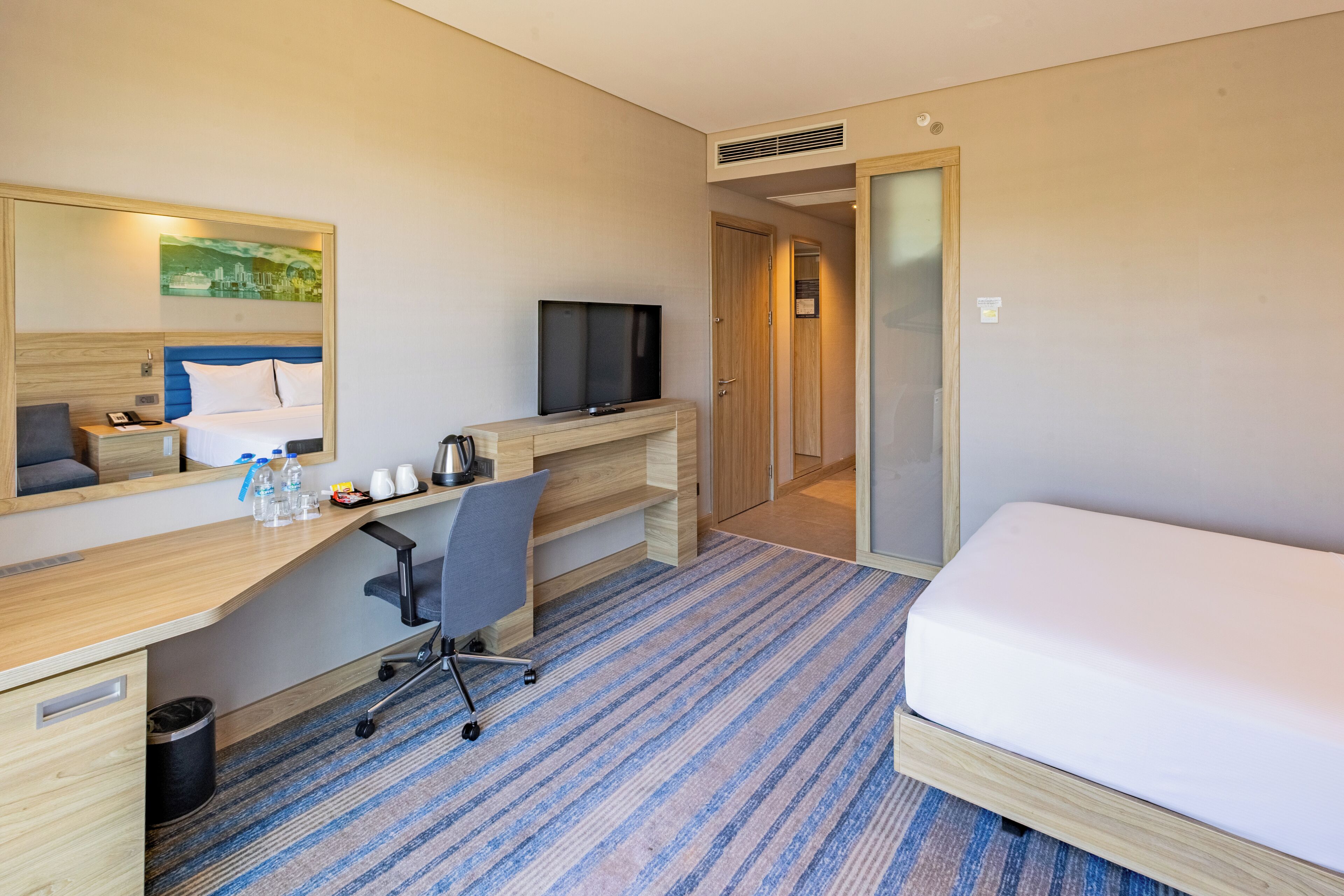 Una habitación de hotel con una cama, un escritorio con computadora, una silla, un televisor y un cuadro en la pared.
