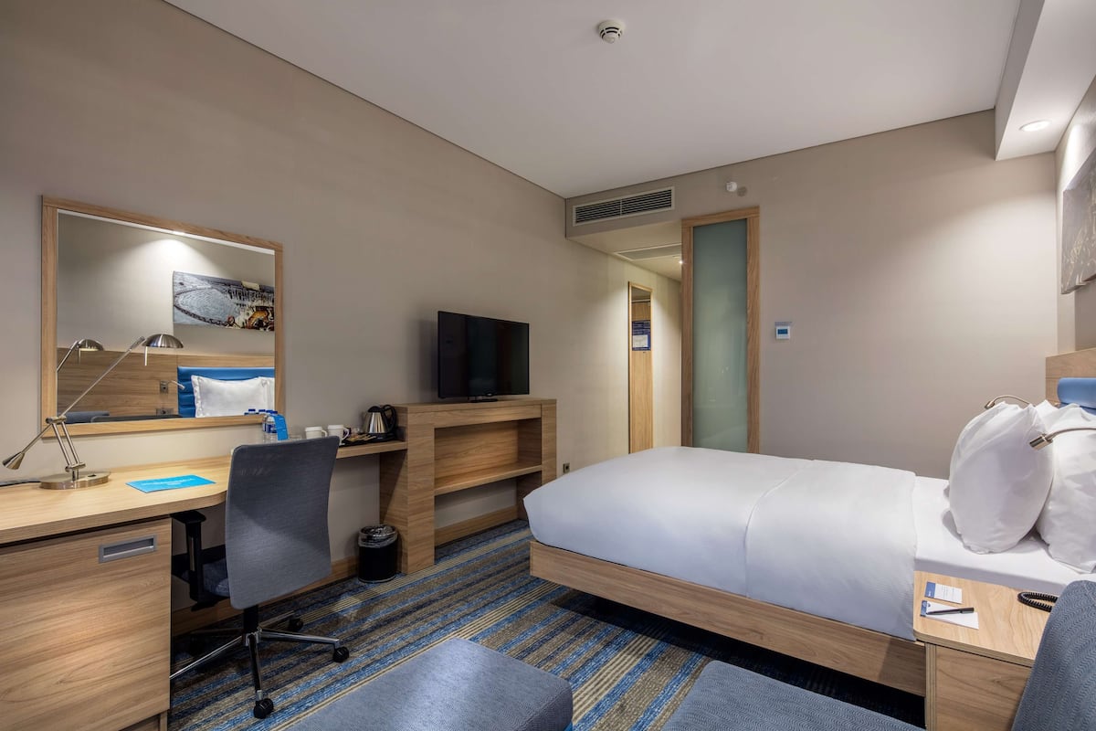 Een hotelkamer met een bed, bureau, stoel, televisie en spiegel.