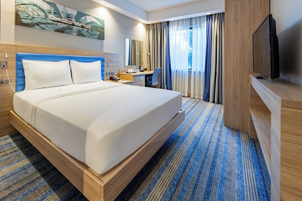Hotelkamer met een groot bed, een bureau, een stoel, een televisie en een raam met gordijnen.