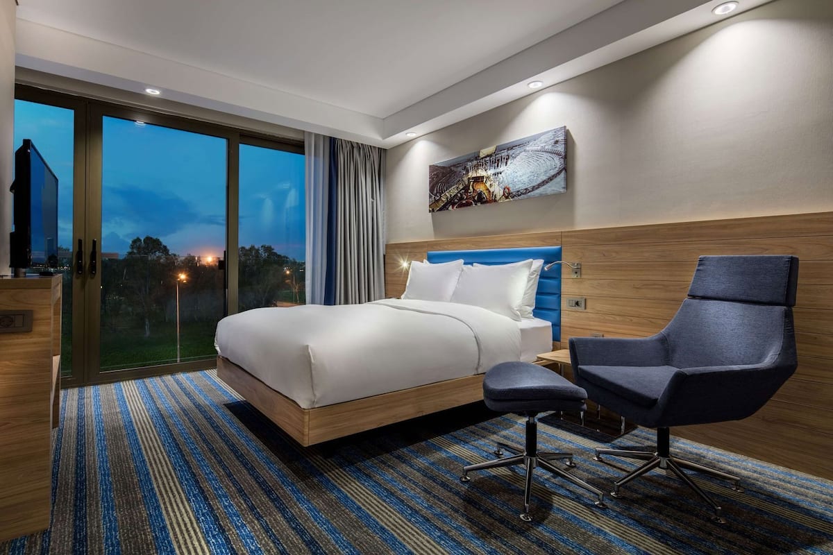 Een moderne hotelkamer met een groot bed, een bureau, een stoel en een schilderij aan de muur.