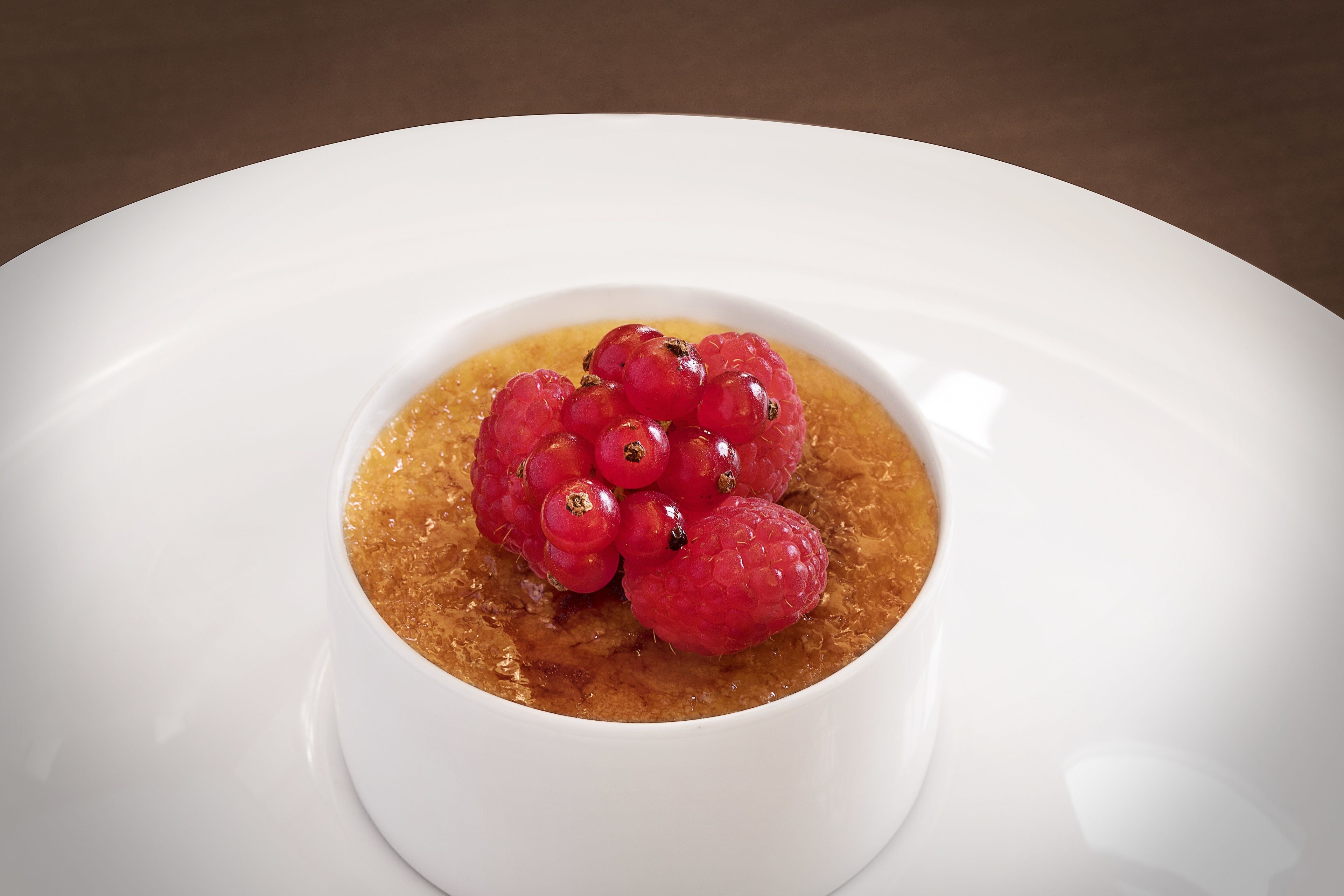 Un bol blanc contenant un dessert brun, surmonté de baies rouges.