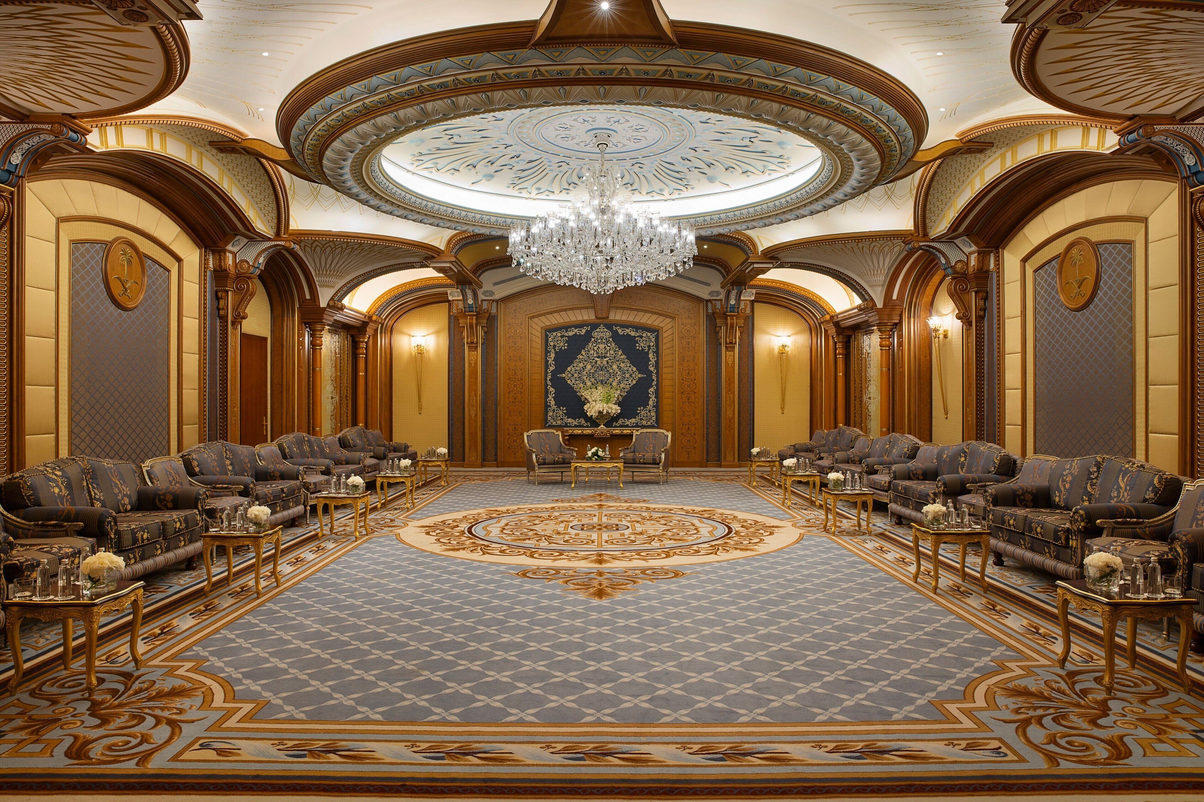 A luxurious room with a grand chandelier, ornate ceiling, and a symmetrical layout of sofas and tables.
