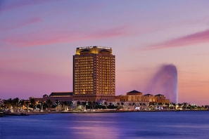 A high-rise hotel with a prominent sign at the top, a waterfront view, and a fountain in the background.