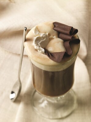 A glass of hot chocolate with whipped cream and chocolate curls on top.
